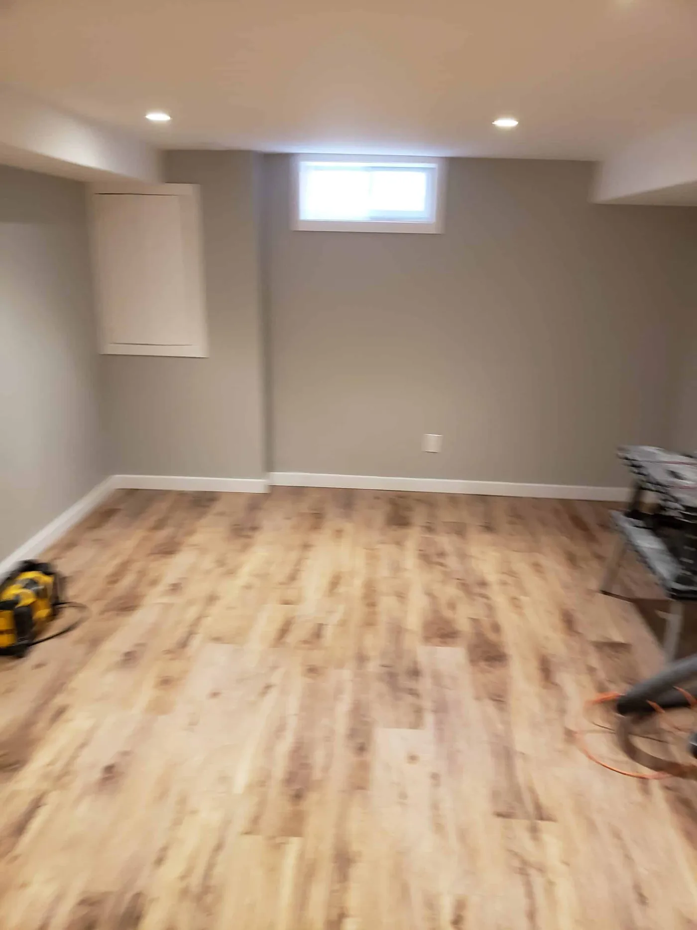 Lower-level room with warm grey walls, white trim and light wood floors