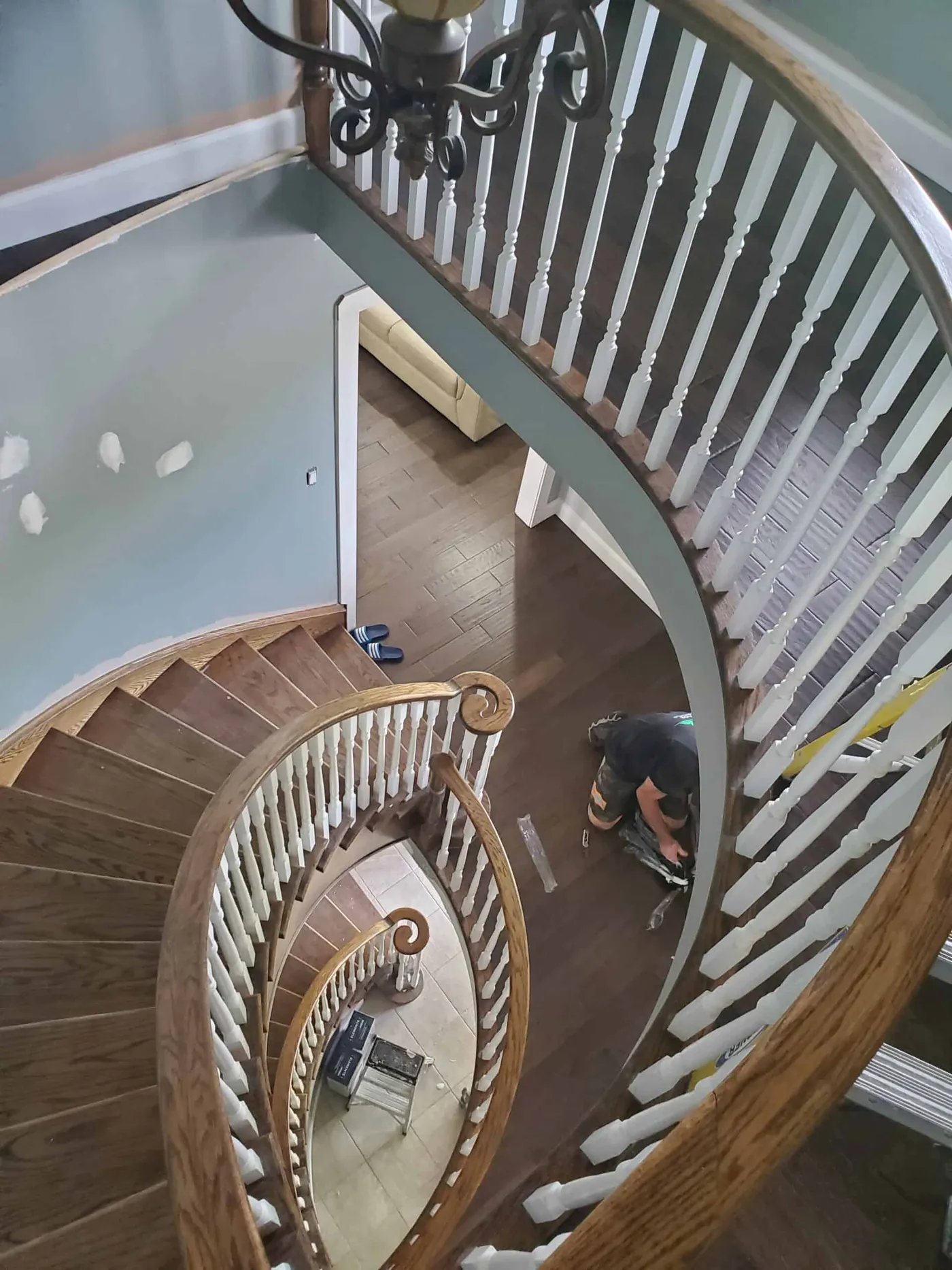 Painter preparing a curved staircase with white spindles and a pale blue wall